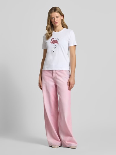 Frauenmodel trägt Regular Fit T-Shirt aus reiner Baumwolle Modell 'KITA' von Only, weiß mit Flamingoprint, Damen T-Shirt, Ganzkörperansicht von vorne.