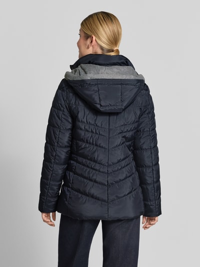 Vrouwenmodel draagt Jacke in Stepp-Optik mit Kapuze van FUCHS SCHMITT in donkerblauw met stiksels, gevoerde opstaande kraag, steekzakken met ritssluiting, getailleerd pasvorm, ruglengte maat 36: 74 cm, schouderbreedte 40 cm, borstwijdte 48 cm, mouwlengte 64 cm, geheel van achteren