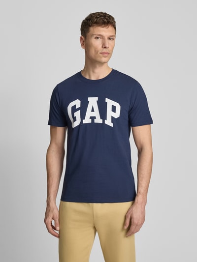 Männermodel trägt T-Shirt mit Logo und Rundhalsausschnitt von GAP in Dunkelblau, Reine Baumwolle, Regular-Fit, Rückenlänge 72 cm, Ganzkörperansicht von vorne.