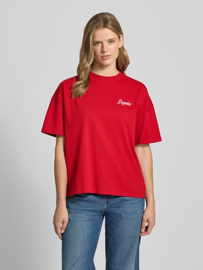 Vrouwenmodel draagt rood oversized T-shirt met labelprint, Pegador Oversized T-shirt mit Label-Print Modell 'RAUMA', puur katoen, ronde hals, ruglengte maat S 60 cm, Ganzkörperansicht van voren.