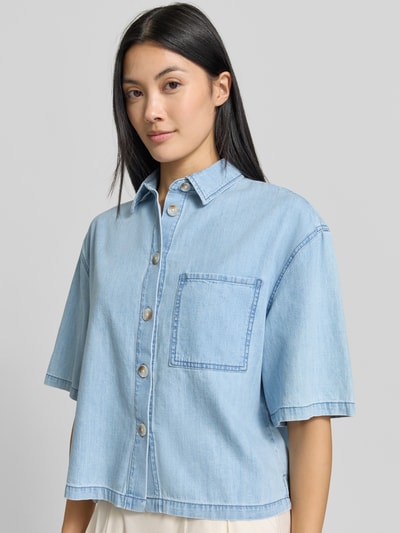 Frauenmodel trägt Relaxed Fit Kurzarmbluse aus reiner Baumwolle von s.Oliver RED LABEL in hellem Blau mit sichtbarer Knopfleiste, Nahaufnahme Oberkörper.