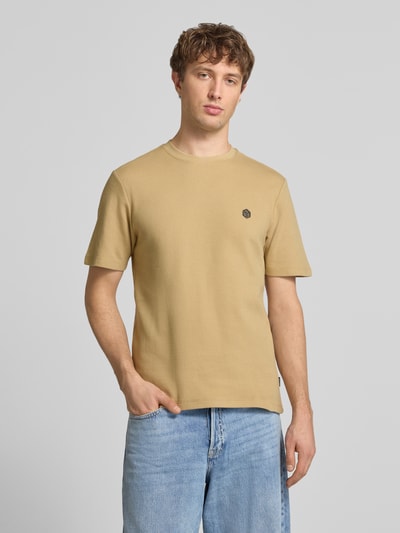 Mężczyzna nosi męski t-shirt z bawełny w kolorze beżowym z detalem z logo, prosty krój, model 'FILLIP' od Blend, okrągły dekolt, długość tyłu w rozmiarze M: 69 cm, zdjęcie całej sylwetki z przodu.