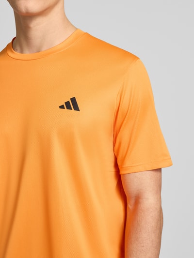 Männermodel trägt T-Shirt mit Logo und Rundhalsausschnitt von adidas Training in Orange, Regular Fit, Nahaufnahme Oberkörper.