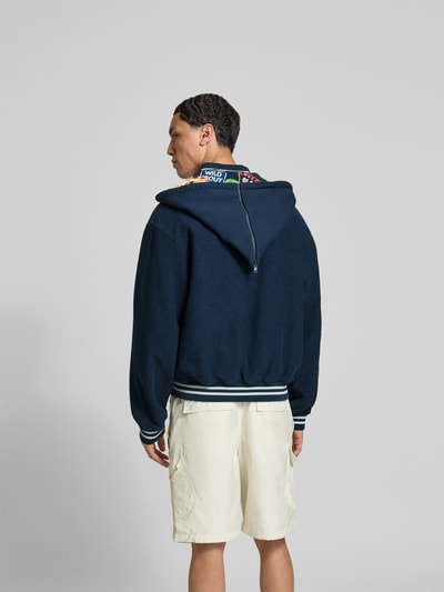 Männermodel trägt Relaxed Fit Jacke mit Motiv-Patches von Kenzo in Dunkelblau aus Baumwolle, Reißverschluss, aufgesetzte Taschen, Ganzkörperansicht Rückansicht