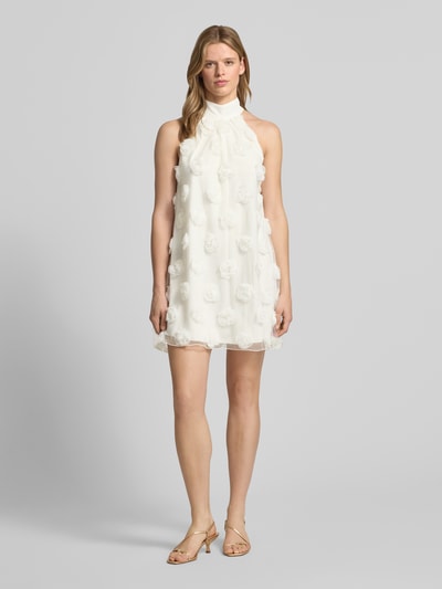Vrouwenmodel draagt Minikleid met florale Applikationen van Gina Tricot in wit, loose fit, halter, druppelvormige hals, ganzlichaamsvooraanzicht.