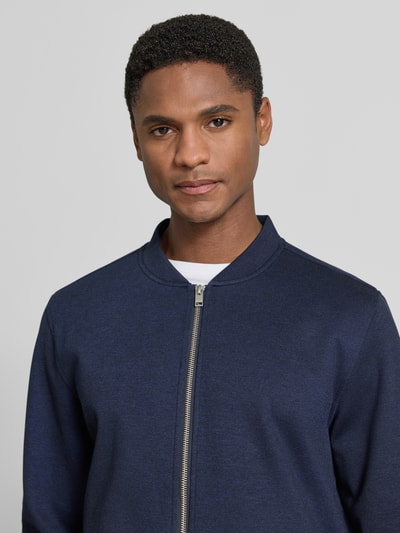Męski model nosi Regular Fit Sweatjacke mit Stehkragen od Lindbergh, elastyczna mieszanka materiałów, zamek błyskawiczny, wpuszczane kieszenie, granatowy kolor, długość tyłu w rozmiarze M: 69 cm, długość rękawów w rozmiarze M: 66 cm, ujęcie: zbliżenie górnej części ciała.