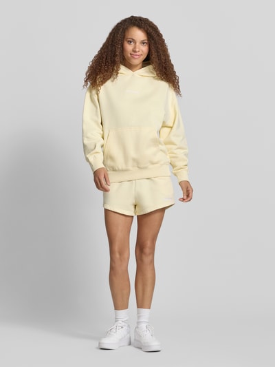 Frauenmodel trägt Oversized Hoodie mit Label-Stitching Modell 'CLARITA' von Pegador aus Baumwoll-Mix in Hellgelb, Känguru-Tasche, Ganzkörperansicht von vorne.