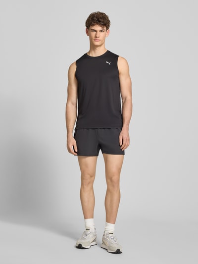 Männermodel trägt Top mit Logo und Rundhalsausschnitt von PUMA PERFORMANCE in Schwarz, glatte Textur, Regular Fit, Ganzkörperansicht von vorne.
