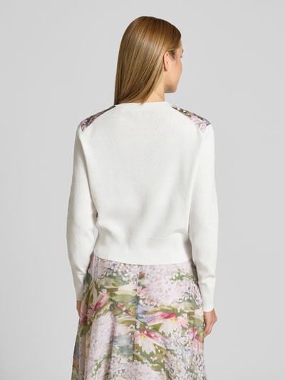Frauenmodel trägt Cardigan mit geripptem Rundhalsausschnitt Modell 'SISILLA' von Ted Baker in Weiß mit floralem Muster an den Schultern, gerader Schnitt, gerippte Abschlüsse, Rückenlänge 48 cm, Ärmellänge 61 cm, Ganzkörperansicht Rückansicht.