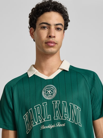 Männermodel trägt Regular Fit T-Shirt mit Umlegekragen von KARL KANI in Grün mit Logo-Stitching, Kurzärmelig, Nahaufnahme Oberkörper. Herren T-Shirt, Rückenlänge bei Größe M: 67 cm.