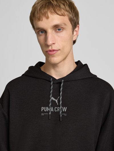 Männermodel trägt Hoodie mit Logo von PUMA PERFORMANCE, schwarz, Material-Mix mit Lyocell-Anteil, Relaxed Fit, Nahaufnahme Oberkörper.