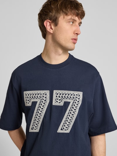 Männermodel trägt T-Shirt mit Ketten-Stickerei und Rundhalsausschnitt von REVIEW aus reiner Baumwolle im Relaxed-Fit, Nahaufnahme Oberkörper.