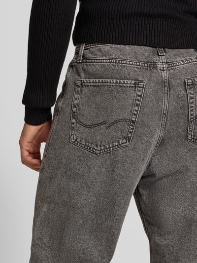 Männermodel trägt Baggy Jeans im 5-Pocket-Design Modell 'ALEX' von JACK & JONES aus bawełna, krój baggy, zapięcie na guzik i zamek błyskawiczny, 5 kieszeni, Szerokość w rozmiarze 32/32: 42 cm, Długość wewnętrzna nogawki w rozmiarze 32/32: 74 cm, szara sprana faktura, widoczne tylne kieszenie, Ganzkörperansicht Rückansicht