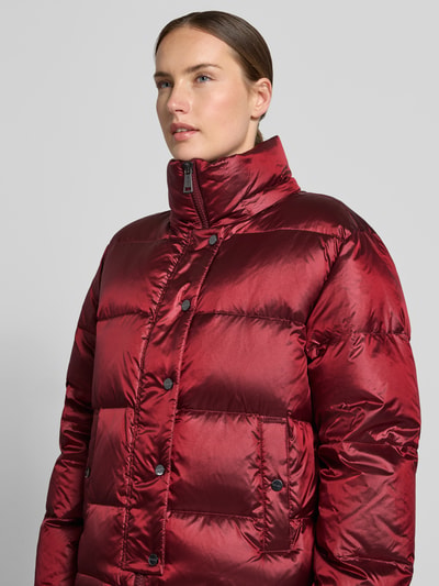 Kobieta modelka ma na sobie Regular Fit kurtkę z wypełnieniem z puchu i pierza Model 'Jilly' od MOS MOSH, efekt pikowania, bordowy kolor, z kapturem z tunelem, Długość tyłu w rozmiarze S: 62 cm, szerokość ramion w rozmiarze S: 47 cm, szerokość w klatce piersiowej w rozmiarze S: 54 cm, długość rękawów w rozmiarze S: 65 cm, zdjęcie zbliżenie na górną część ciała.