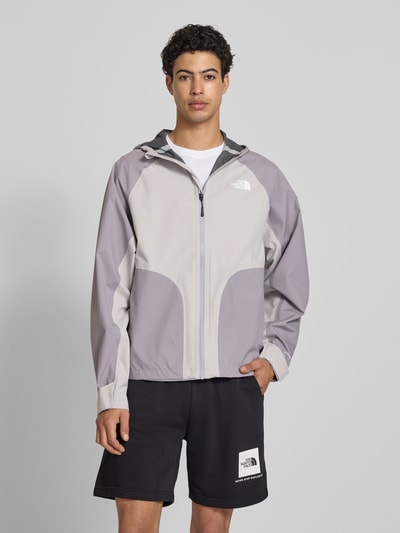 Männermodel trägt Regenjacke mit Logo von The North Face in Grau mit Kapuze und Reißverschluss, Regular Fit, Ganzkörperansicht von vorne. Rückenlänge bei Größe M: 70 cm, Schulterbreite: 50 cm, Brustweite: 62 cm, Ärmellänge: 76 cm.