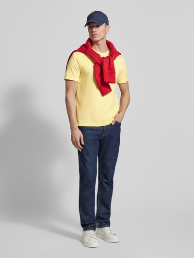 Mannenmodel draagt Regular Fit T-Shirt aus reiner Baumwolle van Tommy Hilfiger, uni geel, logo-stitching, ronde hals, korte mouw, jersey, katoen. Volledig lichaamsaanzicht van voren.