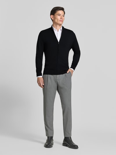 Männermodel trägt Slim Fit Strickjacke aus Viskose-Mix mit Stehkragen von MCNEAL in Schwarz, graue Hose, Ganzkörperansicht von vorne. Kontext: Herren Strickjacke, Viskose-Mix, Slim Fit, Stehkragen, Reißverschluss, elastische Abschlüsse, Rückenlänge 70 cm, Ärmellänge 70 cm.