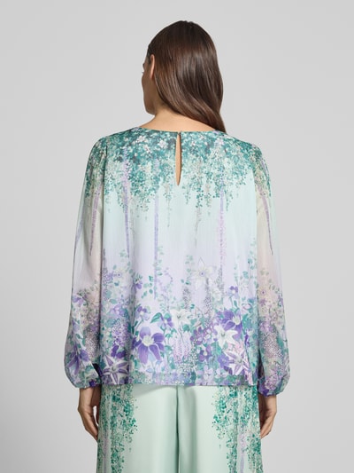 Frauenmodel trägt Regular Fit Bluse mit Rundhalsausschnitt von Marc Cain, Schimmernd, Allover-Look, Knopfverschluss, Rückenlänge 60 cm, Ärmellänge 64 cm, zarte Farbverläufe in Grün und Lila, florale Muster, fließender Stoff, Ganzkörperansicht Rückansicht.