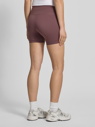Frauenmodel trägt Radlerhose mit Logo und elastischem Bund von NIKE TRAINING in Mauve, Material-Mix mit Stretch-Anteil, körpernahe Passform, Logo, Elastischer Bund, Bundweite bei Größe S: 27 cm, Innenbeinlänge bei Größe S: 12 cm, Ganzkörperansicht Rückansicht.