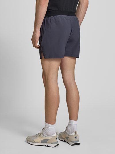 Männermodel trägt Regular Fit Shorts mit Logo-Print von PUMA PERFORMANCE in Dunkelgrau, glatte Textur, elastischer Bund, Ganzkörperansicht Rückansicht. Elastischer Material-Mix, Eingrifftaschen, sportlicher Look.