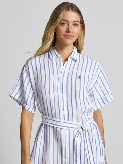 Modelka kobieca ma na sobie Oversized Hemdblusenkleid aus reinem Leinen od Lauren Ralph Lauren w biało-niebieskie paski, logo na piersi, pasek w talii, flammowana struktura lnu, optyka two tone, krótki rękaw, krój oversized, dekolt w serek, długość midi; zbliżenie na górną część ciała.