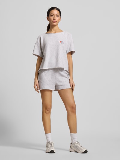 Modelka nosi Sweatshorts mit elastischem Bund Modell 'TUBAY' von American Vintage, bawełna z domieszką elastanu, prosty krój, kieszeń tylna, kieszenie boczne, elastyczny pas, długość nogawki wewnętrznej w rozmiarze S: 9 cm, kolor jasnoszary, gładka tekstura, całkowity widok z przodu.