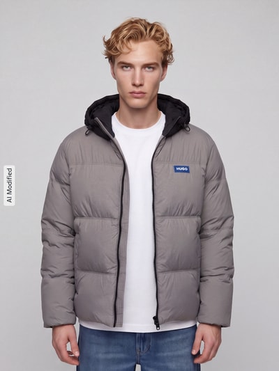 Mężczyzna nosi Regular Fit Steppjacke mit Kapuze Modell 'Bodo2541' von HUGO, szara dwukolorowa popelina, naszywka z logo, wpuszczane kieszenie, hydrofobowy, długi rękaw, elastyczne wykończenie, Ganzkörperansicht von vorne, KI-modifiziertes Bild.