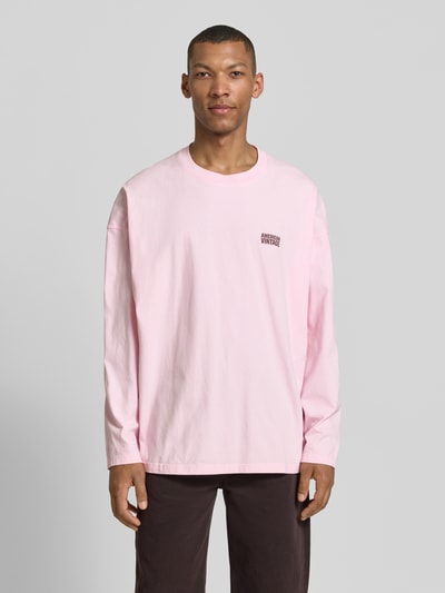 Männermodel trägt Longsleeve mit Logo-Print Modell 'GIXY' von American Vintage in Rosa, Reine Baumwolle, Loose-Fit, Ganzkörperansicht von vorne.