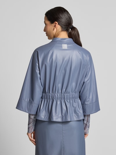 Frauenmodel trägt Blazer in Leder-Optik mit Stehkragen von Marc Cain, taillierte Passform, 3/4-Arm, glänzende Oberfläche, Ganzkörperansicht Rückansicht.