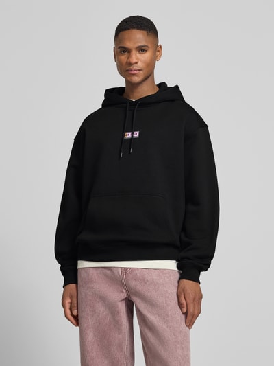 Męski model nosi Hoodie mit Logo-Print Modell 'Chase' od Les Deux, czarny, bawełna, luźny krój, z kapturem, przód, zdjęcie całej sylwetki.