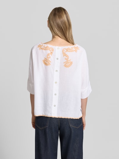 Frauenmodel trägt Blusenshirt mit Leinen-Anteil und Motiv-Stitching von Christian Berg Woman, weiß mit orangen Details, Viskose-Mix, Loose-Fit, U-Boot-Ausschnitt, Rückenlänge 55 cm, Ärmellänge 34 cm, Ganzkörperansicht Rückansicht.