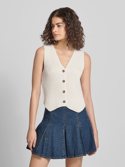 Modelka nosi Shaped Fit Weste aus reiner Baumwolle von Marc O'Polo Denim, kremowa, gładka, dzianinowa, bez kołnierza, z warkoczowym wzorem, z asymetrycznym dołem, z bawełny, zapięcie na guziki, zdjęcie całej sylwetki z przodu.