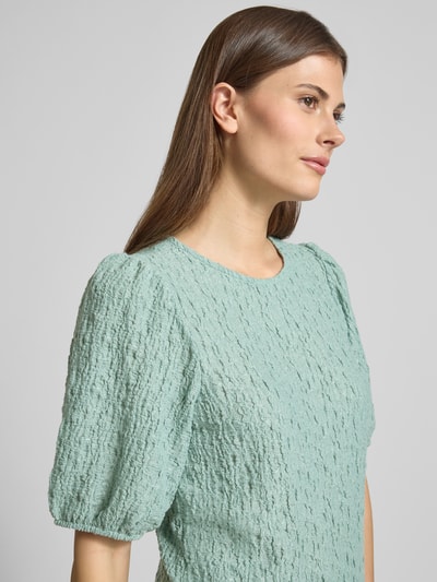 Frauenmodel trägt Blusenshirt mit Strukturmuster Modell 'FALL' von Vila in mintgrünem Strukturmuster, Material-Mix mit Stretch-Anteil, Regular-Fit, Rundhalsausschnitt, Nahaufnahme Oberkörper. Rückenlänge bei Größe S: 53 cm, Ärmellänge bei Größe S: 31 cm.