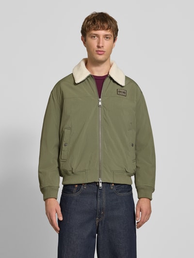 Männermodel trägt Regular Fit Bomberjacke mit abnehmbarem Teddy-Kragen von Tommy Jeans in Olivgrün, Herren Bomberjacke, Ganzkörperansicht von vorne.
