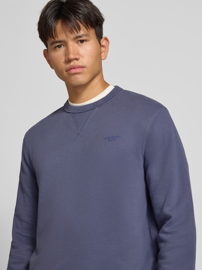 Männermodel trägt Sweatshirt aus Baumwoll-Mix von Superdry in Blau mit Rundhalsausschnitt, Label-Stitching, Nahaufnahme Oberkörper.
