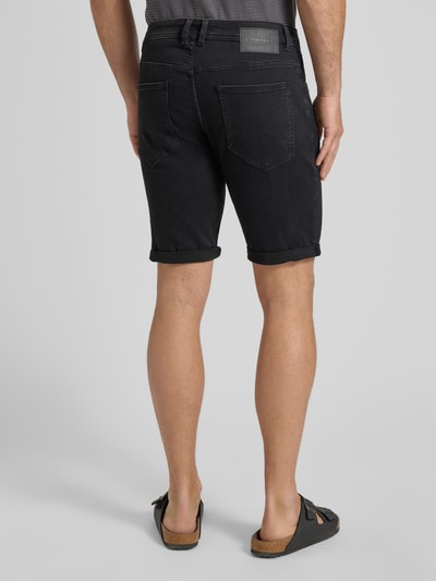 Mannenmodel draagt Regular Fit Jeans Bermudas uit katoenmix van Tom Tailor in zwarte denimlook met label patch, vijf-zakken ontwerp, slim leg, knoop en verborgen ritssluiting, riemlussen, geheel achteraanzicht.