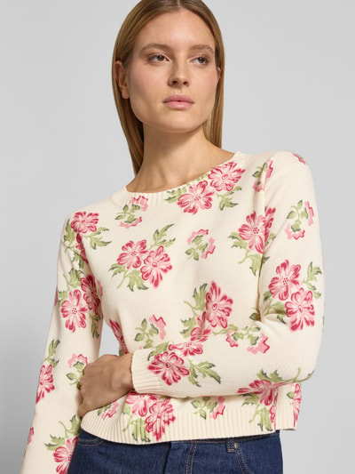 Frauenmodel trägt Boxy Fit Strickpullover aus reiner Baumwolle Modell 'EDITTO' von Weekend Max Mara mit floralem Muster, Strickoptik, Rundhals, Langarm, gerippten Abschlüssen, in Creme mit rosa und grünen Farbakzenten, Ganzkörperansicht von vorne.