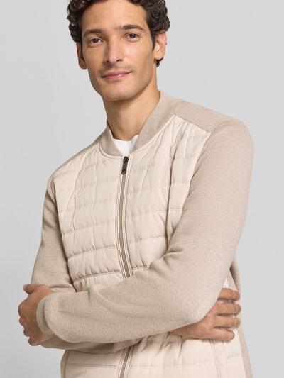 Mężczyzna nosi Strickjacke mit Stehkragen und Steppnähten od ROY ROBSON w beżowym kolorze, bawełna z wiskozą, krój regular fit, z dwukierunkowym suwakiem i kieszeniami na ręce, długość tyłu 74 cm, długość rękawa 74 cm, zdjęcie: zbliżenie górnej części ciała z przodu.