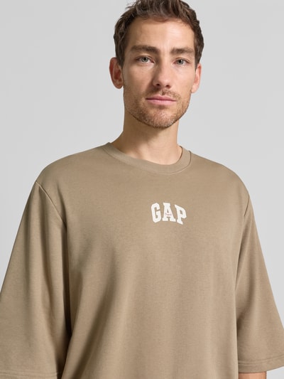Männermodel trägt T-Shirt mit Rundhalsausschnitt und Logo-Print van GAP in beige katoenmix, loose fit, ribboorden, Nahaufnahme Oberkörper