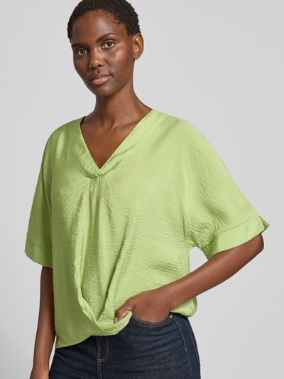 Frauenmodel trägt Blusenshirt mit V-Ausschnitt von Christian Berg Woman in Hellgrün mit 1/2-Arm, Drapierung, Regular-Fit, Nahaufnahme Oberkörper. Rückenlänge bei Größe 36: 31 cm, Ärmellänge bei Größe 36: 61 cm.