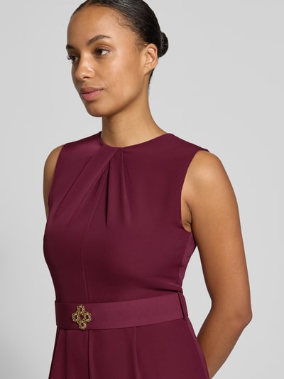 Frauenmodel trägt Jumpsuit mit Stoffgürtel von Rinascimento in dunklem Rot, Material-Mix mit Stretch, Nahaufnahme Oberkörper.
