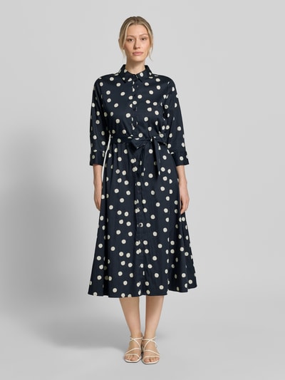 Modelka kobieca nosi Regular Fit Blusenkleid aus Baumwoll-Mix od s.Oliver BLACK LABEL, granatowa tkanina, białe grochy, midi, pasek, krój regular fit, długi rękaw, materiał bawełniany, widok całej sylwetki z przodu.