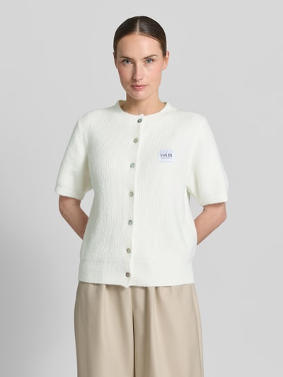 Frauenmodel trägt Regular Fit Strickjacke aus Viskose-Mix Modell 'MONA' von VILLA SOPHIE, Optik: Unifarben, einreihige Knopfleiste, Label-Applikation, Rundhals, Kurzarm, gerippter Rumpf- und Ärmelabschluss, Materialverarbeitung: Strick, Ganzkörperansicht von vorne.