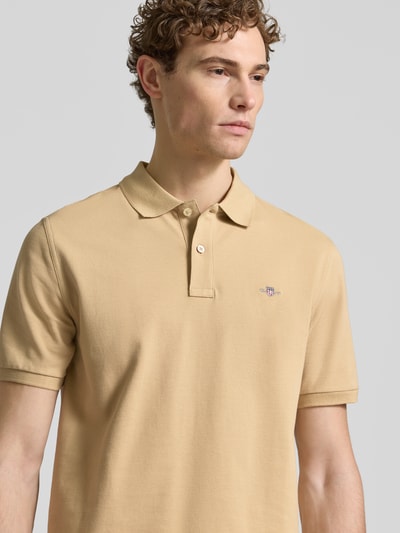 Männermodel trägt Slim Fit Poloshirt mit Logo-Stitching von Gant in Beige, reine Baumwolle, Polo-Kragen, Nahaufnahme Oberkörper.