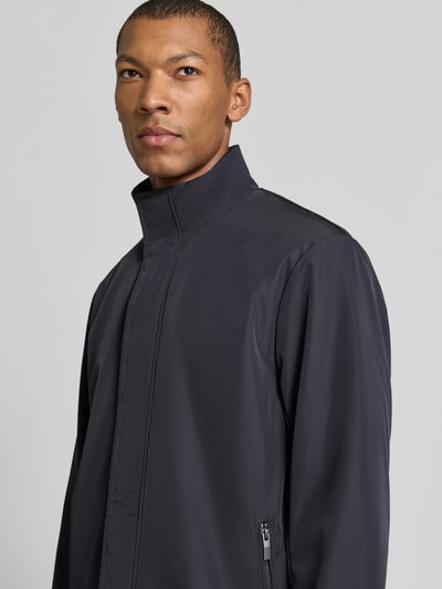 Männermodel trägt Trenchcoat mit verdecktem Reißverschluss von Armani Exchange in Dunkelblau, glatte Oberfläche, Nahaufnahme Oberkörper. Regular Fit, Stehkragen, Reißverschlusstaschen, Maße Größe M: Rückenlänge 85 cm, Schulterbreite 45 cm, Brustweite 50 cm, Ärmellänge 65 cm