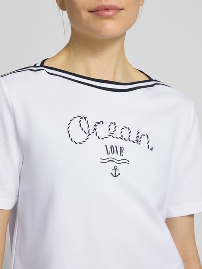 Kobiece model prezentuje T-Shirt mit Kontraststreifen und Print od Marc Cain, bawełna z elastanem, krój regular fit, nadruk i kontrastowe paski, długość pleców w rozmiarze 36: 55 cm, zbliżenie na górną część ciała.