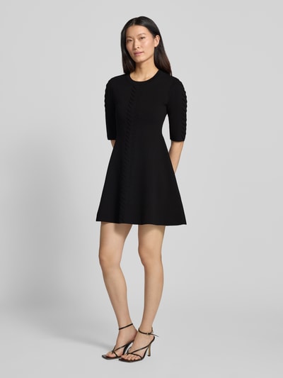 Frauenmodel trägt Minikleid aus Viskose-Mix Modell 'Abito Maglia' von Liu Jo White in Schwarz mit Zierbesatz, leicht ausgestellt, Ganzkörperansicht von vorne.