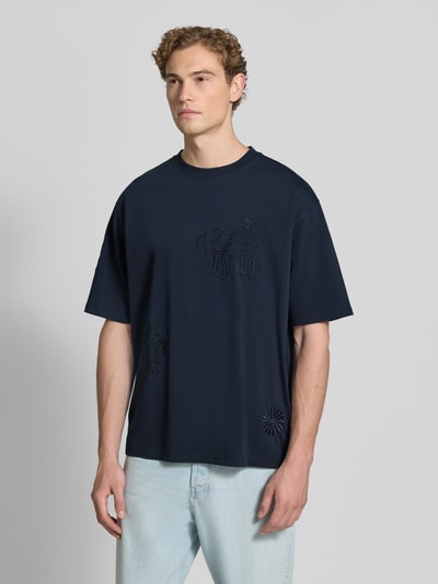 Männermodel trägt T-Shirt mit Stitchings und Rundhalsausschnitt von Scotch & Soda in Dunkelblau, relaxed Fit, reine Baumwolle, Ganzkörperansicht von vorne.
