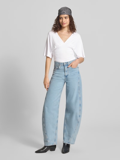 Frauenmodel trägt Bluse aus Viskose-Mix mit V-Ausschnitt von Gina Tricot in Weiß mit taillierter Passform, Halbarm, Ganzkörperansicht von vorne.