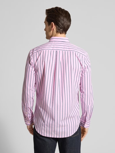 Męski model nosi Regular Fit Freizeithemd aus reiner Baumwolle von Tommy Hilfiger w różowo-granatowe paski, krój regular fit, długi rękaw, popelina, widok całej sylwetki od tyłu.